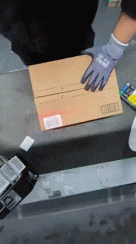 A Person Wearing Gloves Is Holding A Cardboard Box With A Barcode On It GIF