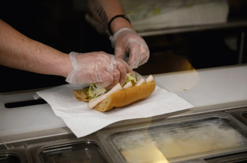 A Person Wearing Plastic Gloves Prepares A Sandwich GIF