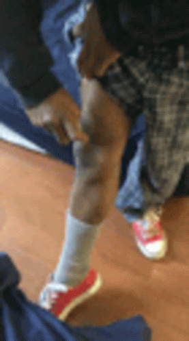A Person Wearing Red Shoes And White Socks Is Standing On A Wooden Floor And Pointing At Their Knee . GIF