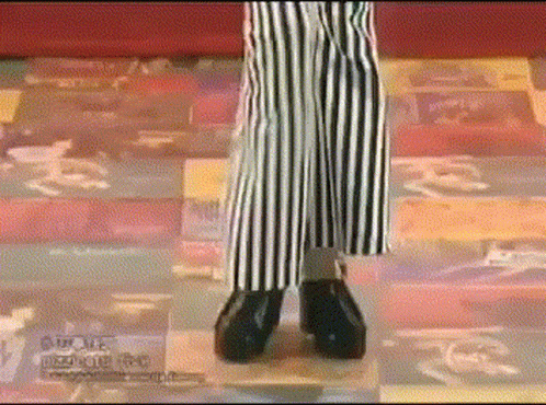A Person Wearing Striped Pants And Black Shoes Is Standing On A Checkered Floor .. GIF