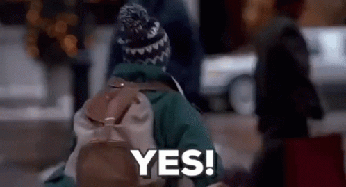 A Person With A Backpack And A Hat Is Walking Down The Street And Saying Yes . GIF