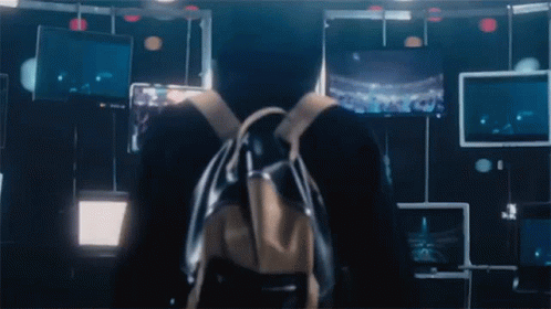A Person With A Backpack Stands In Front Of A Wall With Monitors GIF