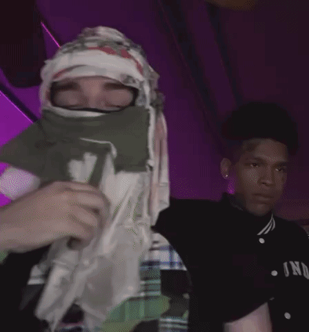 A Person With A Bandana On Their Face Is Holding A Cup With The Letter D On It GIF