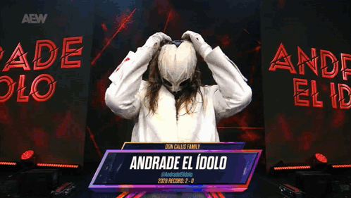 A Person With A Mask On Stands In Front Of A Sign That Reads Andrade El Idolo GIF