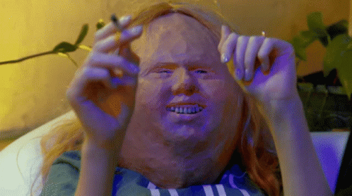 A Person With A Mask On Their Face Is Holding A Cigarette GIF