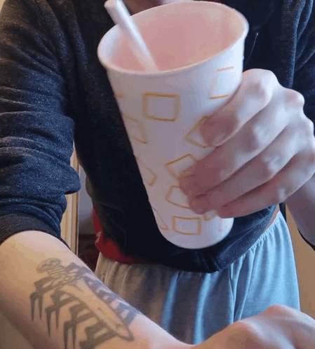 A Person With A Tattoo On Their Arm Holds A Cup With A Straw In It GIF