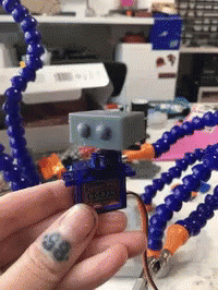 A Person With A Tattoo On Their Finger Is Holding A Robot GIF