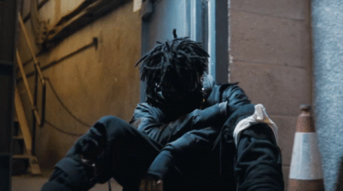 A Person With Dreadlocks Is Sitting On The Ground With Their Head Down GIF