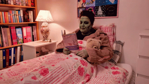 A Person With Green Paint On Their Face Is Reading A Book In A Bed With A Teddy Bear GIF