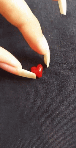 A Person With Long Nails Is Holding A Small Red Heart In Their Hand GIF