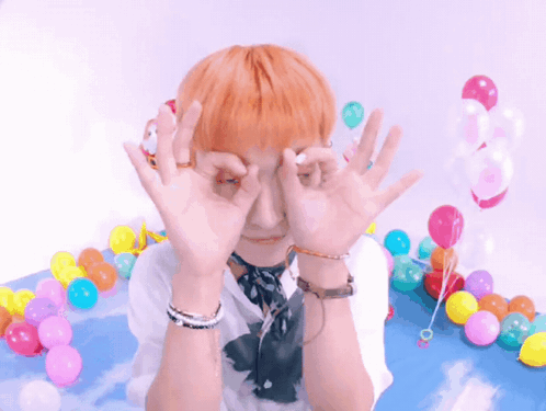 A Person With Orange Hair Covering Their Eyes With Their Hands In Front Of Balloons GIF