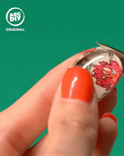 A Person With Red Nails Is Holding A Glass Cabochon With A Floral Design On It In Front Of An Abc Diy Original Logo GIF