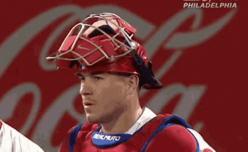 a philadelphia baseball player wearing a helmet with a coca cola logo behind him