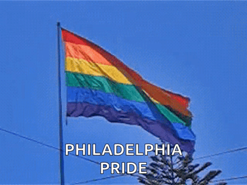 A Philadelphia Pride Flag Is Flying In The Wind Against A Blue Sky GIF