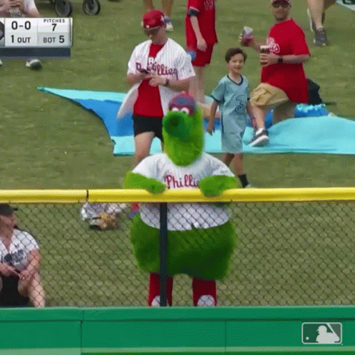 A Phillies Mascot Stands In Front Of A Fence At A Baseball Game GIF