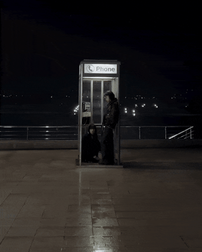 A Phone Booth Is Lit Up At Night With Two People Inside GIF