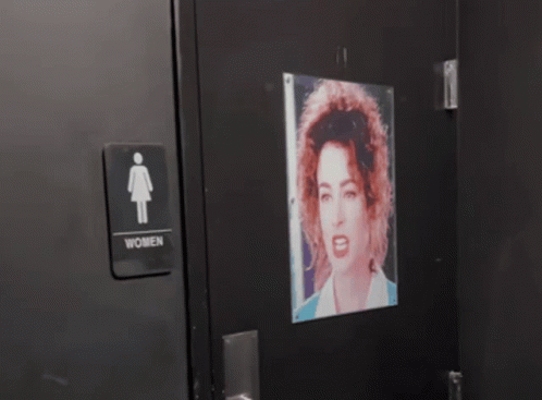 A Picture Of A Man With A Mustache Is Projected On A Wall Next To A Sign For A Men 'S Restroom GIF