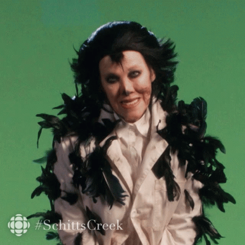 A Picture Of A Woman With Black Feathers Around Her Neck And The Words Schitts Creek GIF