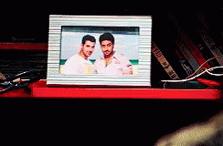 A Picture Of Two Men In A Frame Is On A Red Shelf GIF