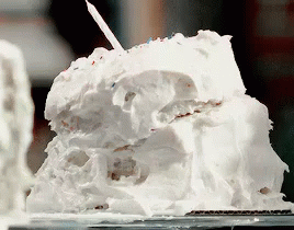 A Piece Of Cake With White Frosting And A Candle On Top GIF