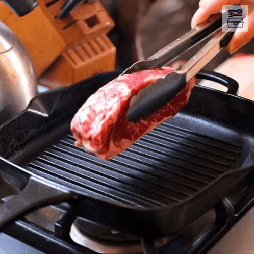 A Piece Of Meat Is Being Cooked In A Pan With Tongs GIF
