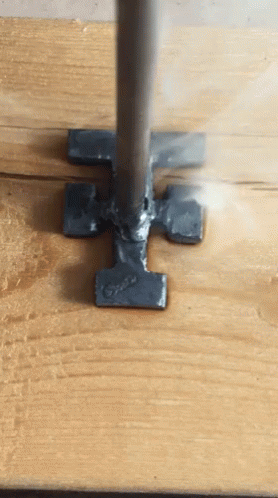 A Piece Of Metal That Looks Like A Hammer Is On A Wooden Surface GIF