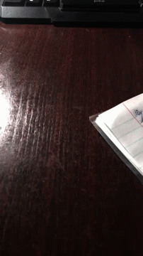 A Piece Of Paper Is Laying On A Wooden Table Next To A Keyboard That Says Dtkc GIF