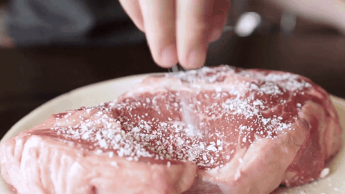 A Piece Of Raw Meat Is Being Seasoned With Salt GIF