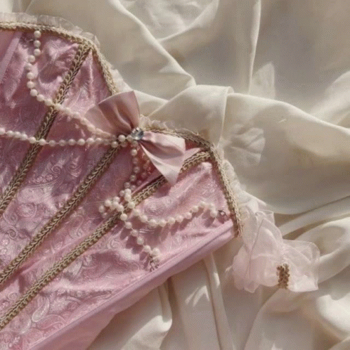 A Pink Corset With Pearls And A Bow On It GIF