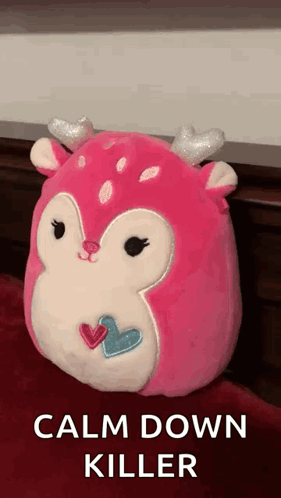 A Pink Deer Stuffed Animal With Hearts On Its Face Is Sitting On A Bed . GIF
