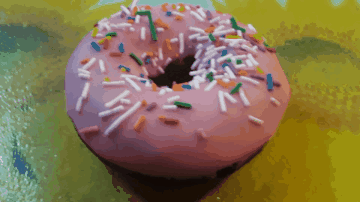 A Pink Donut With Sprinkles On It On A Yellow Surface GIF