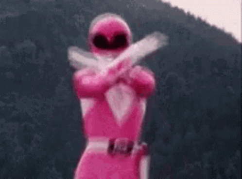 A Pink Power Ranger Is Standing In Front Of A Mountain Holding Two Guns . GIF