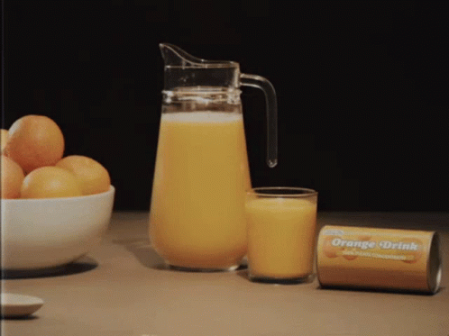 A Pitcher Of Orange Juice Sits Next To A Glass Of Orange Juice And A Can Of Orange Drink GIF