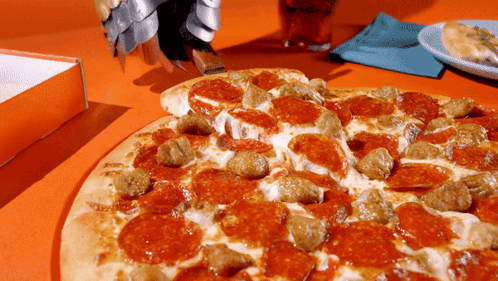 A Pizza With Pepperoni And Sausage Is Sitting On A Table GIF