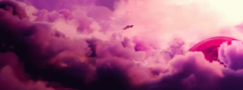 a plane flying through a cloudy sky with a red object in the background