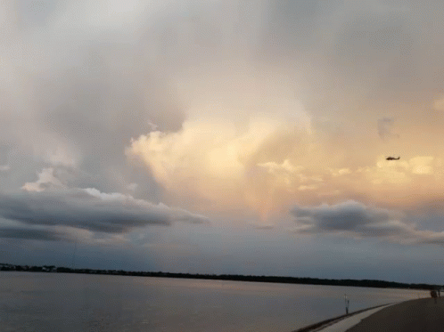 A Plane Is Flying Over A Body Of Water With Clouds In The Sky GIF