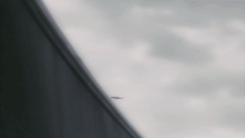 A Plane Is Flying Through A Cloudy Sky Behind A Building GIF