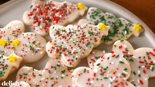 A Plate Of Christmas Cookies With Icing And Sprinkles And The Word Delish On The Bottom GIF