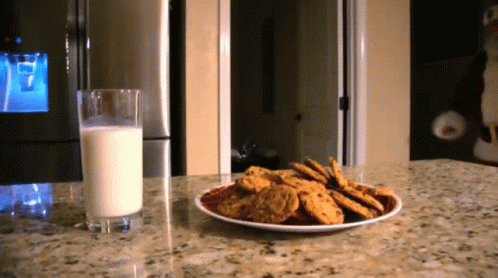 A Plate Of Cookies Next To A Glass Of Milk On A Counter GIF