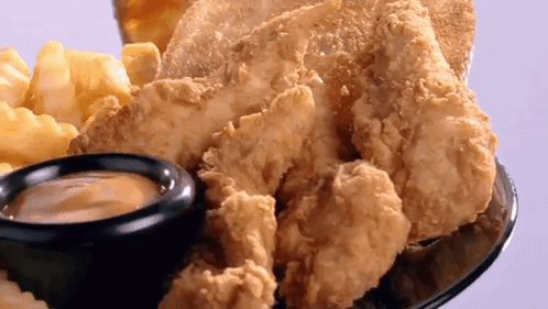 A Plate Of Fried Chicken And French Fries With A Small Bowl Of Dipping Sauce GIF