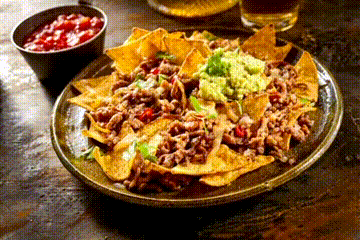 A Plate Of Nachos With Guacamole And Salsa Next To A Bowl Of Salsa On A Table . GIF