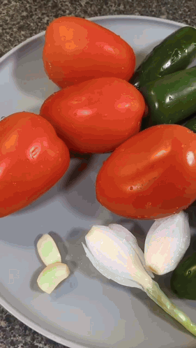 A Plate Of Tomatoes Peppers And Garlic On A Counter Top GIF