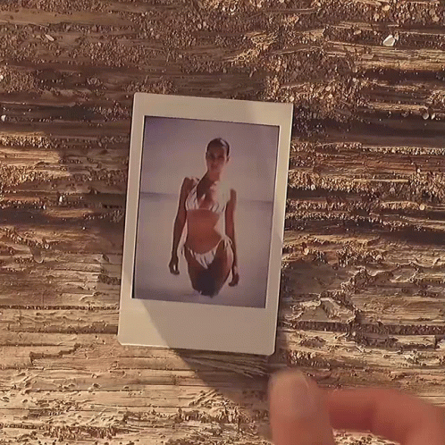 A Polaroid Picture Of A Woman In A Bikini On A Wooden Table GIF