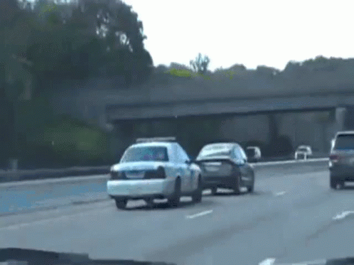 A Police Car Is Driving Down A Highway Next To A Black Car . GIF