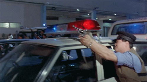 A Police Officer Holds A Gun In Front Of A Police Car GIF