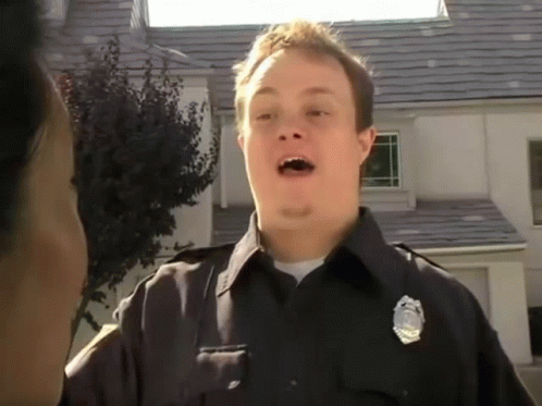 A Police Officer In Front Of A House With A Badge On His Chest GIF