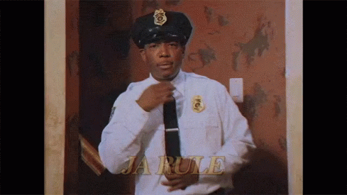 A Police Officer Is Adjusting His Tie In Front Of A Wall That Says Ja Rule GIF