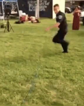 A Police Officer Is Jumping In The Grass . GIF