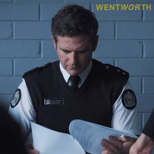A Police Officer Is Looking At A Piece Of Paper With Wentworth Written On The Bottom GIF