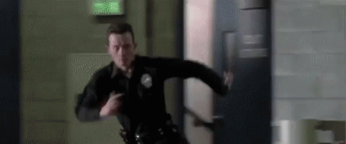 A Police Officer Is Running Through A Hallway With A Gun In His Hand . GIF
